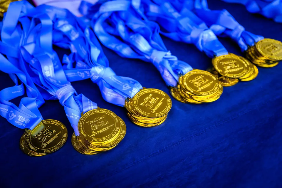 Gold medals on light blue ribbons laid out in stacks on a dark blue table